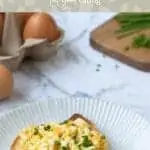 white plate in foreground with piece of toast topped with smashed eggs and garnished with chives. Olive background with text that reads smashed eggs on toast. feel good eating