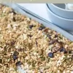 baking tray of nut free granola with white spoon resting on tray. Olive green background with text that reads nut free granola feel good eating