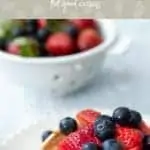 Scalloped plate with stack of pancakes topped with strawberries and blueberries. In the background is a colander with more strawberries and blueberries. Text overlay says What does putting weight loss on the back burner mean? feel good eating