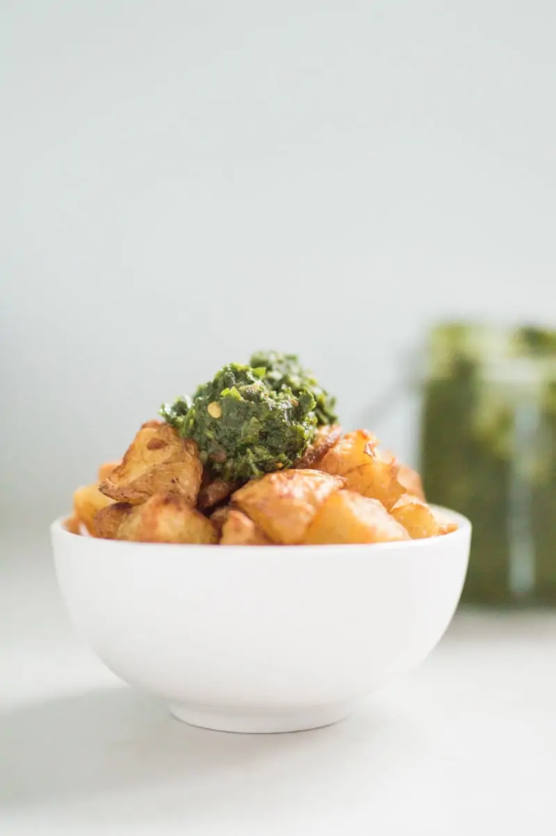 White ceramic bowl filled with crispy paprika roasted potatoes topped with chimichurri
