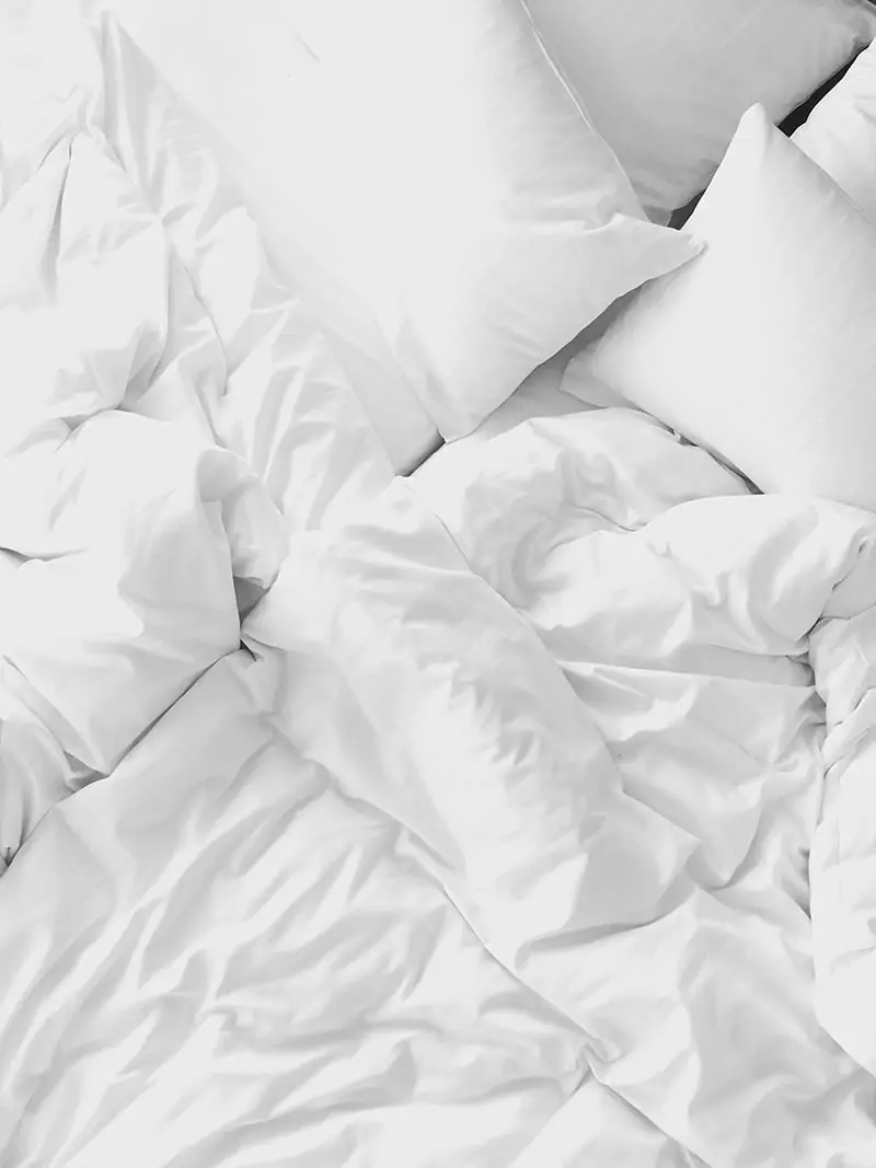 Unmade bed with white pillows and sheets