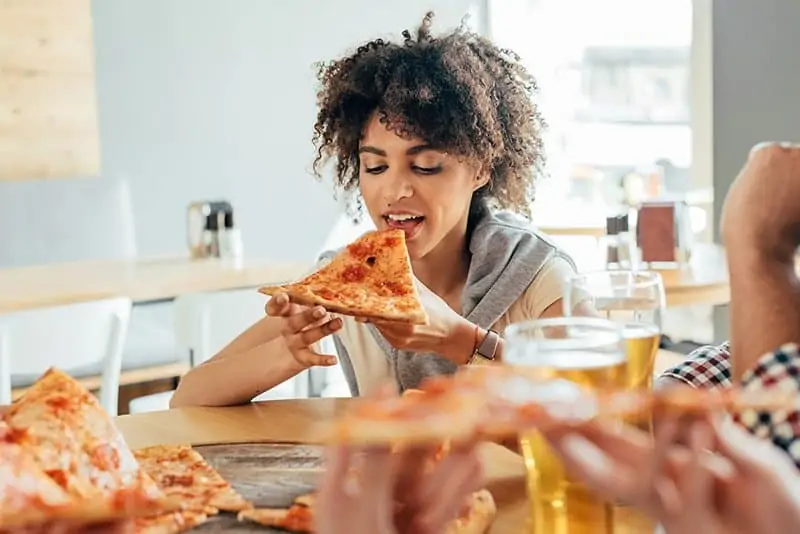 Woman of colour with curly hair about to bite into a slice of pizza