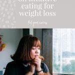 Woman in larger body with brown hair and black t-shirt sitting at a table. She is resting her chin on her hands with a downcast gaze, like she is being contemplative. Purple background with text overlay reads 'the low-down on intuitive eating for weight loss' feel good eating