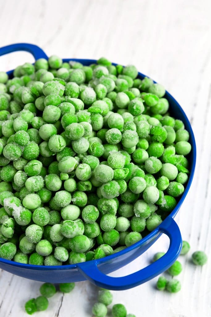 Navy blue colander filled with frozen peas