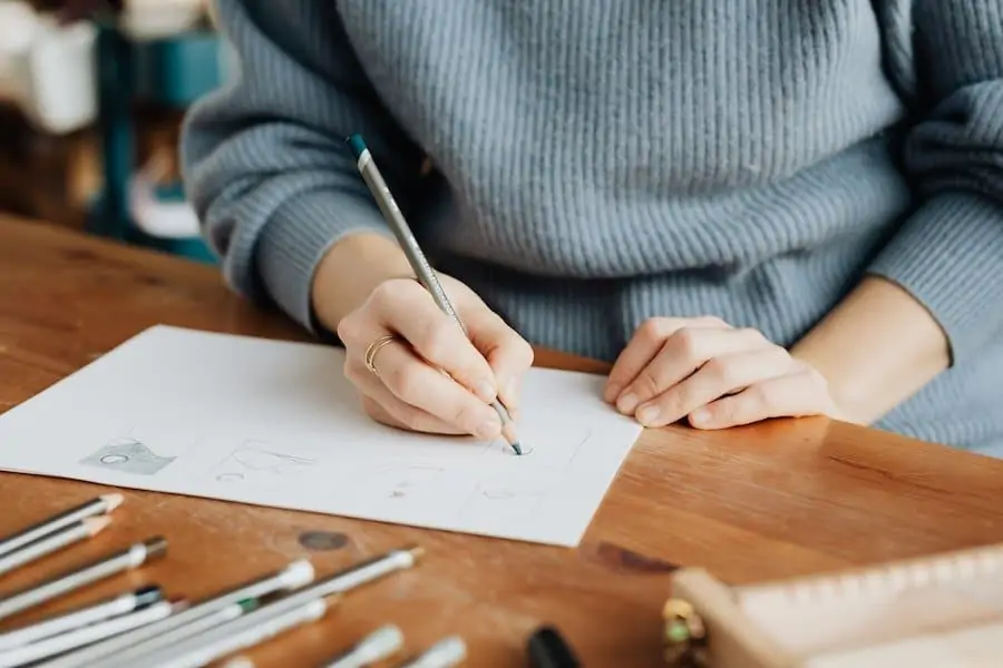 A person in a grey ribbed jumper is sketching. This type of activity can provide a distraction after a binge.