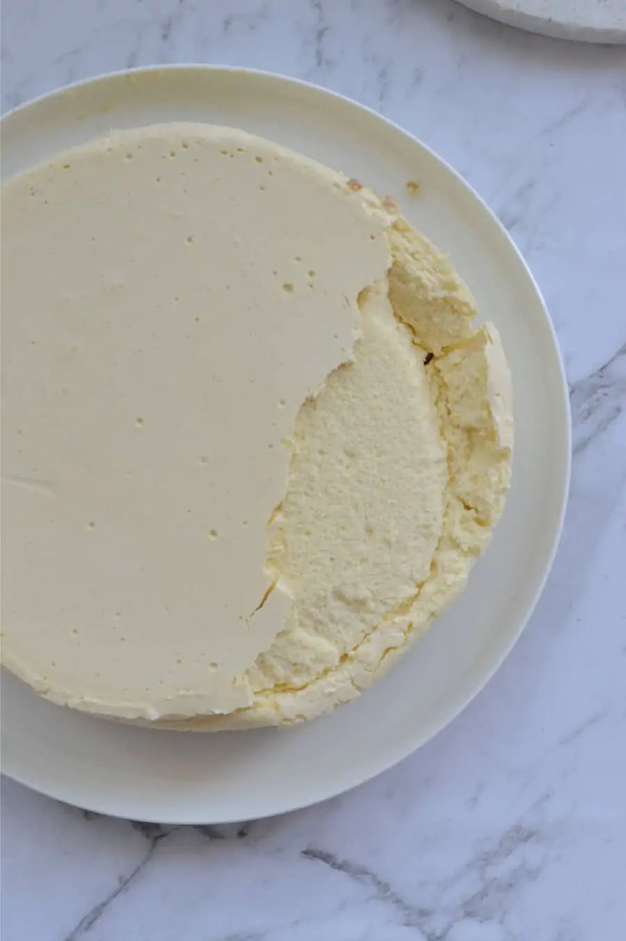 A cheesecake on a plate. One side has collapsed