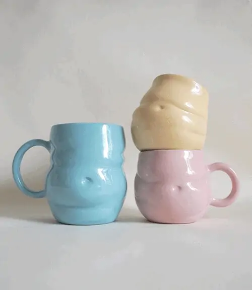 A blue, pink and yellow ceramic mug. They are each shaped in the form of a soft, round belly.