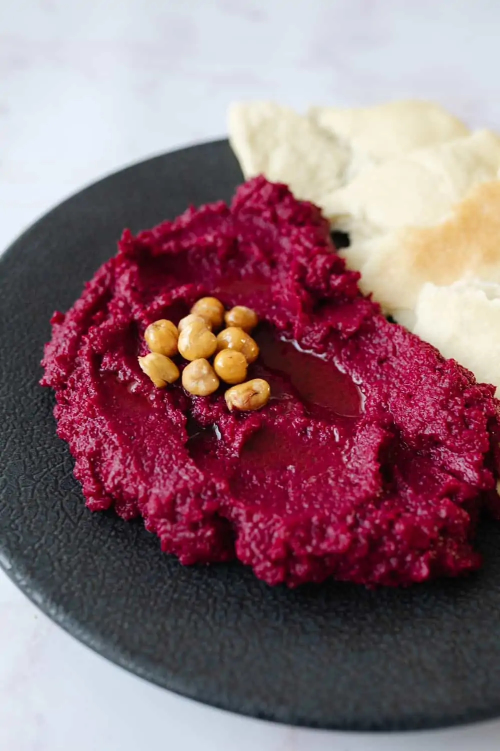Black plate with a pile of roasted beetroot dip on one half and some flatbread on the other half.