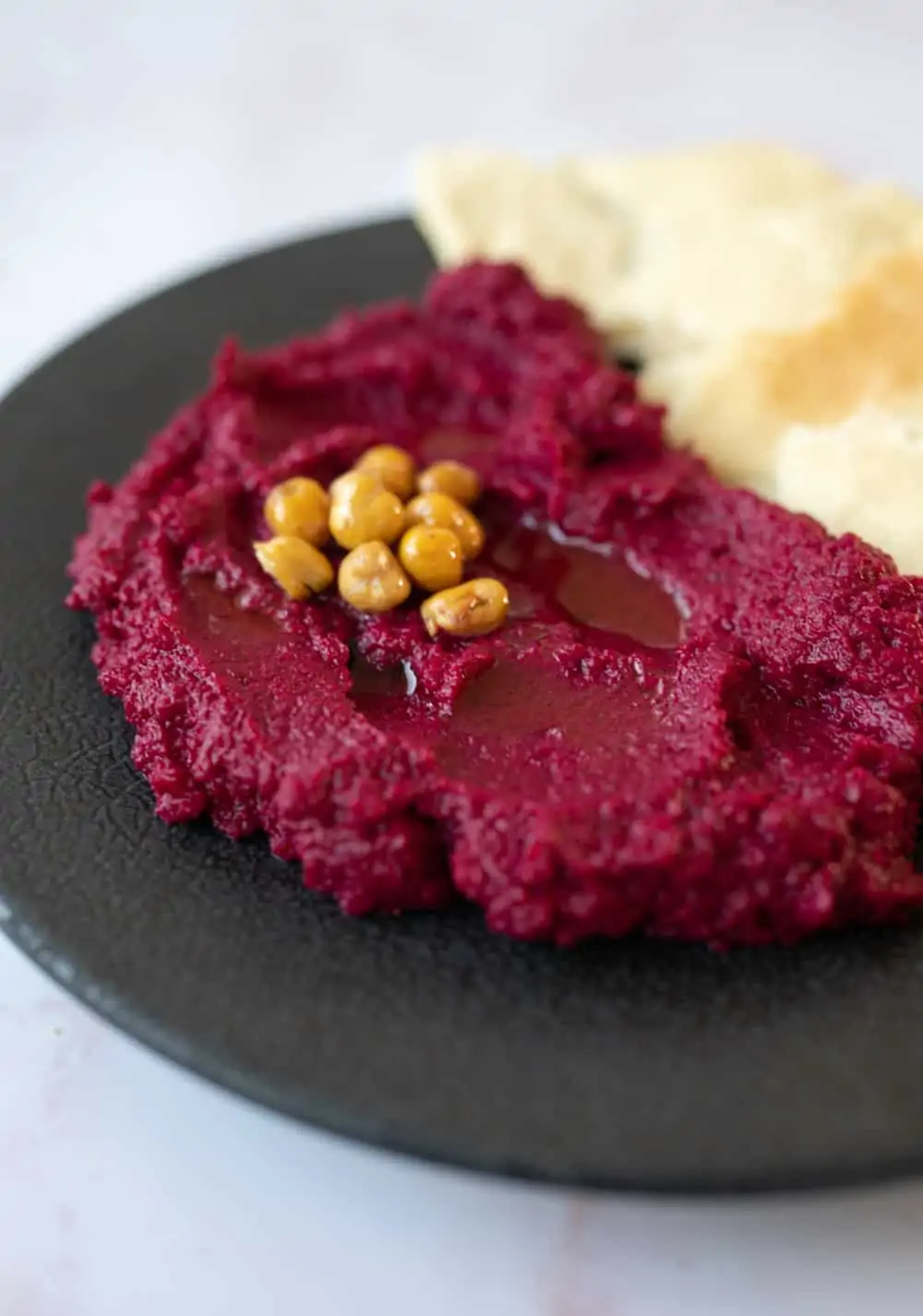 Black plate with a pile of roasted beetroot dip on one half and some flatbread on the other half.