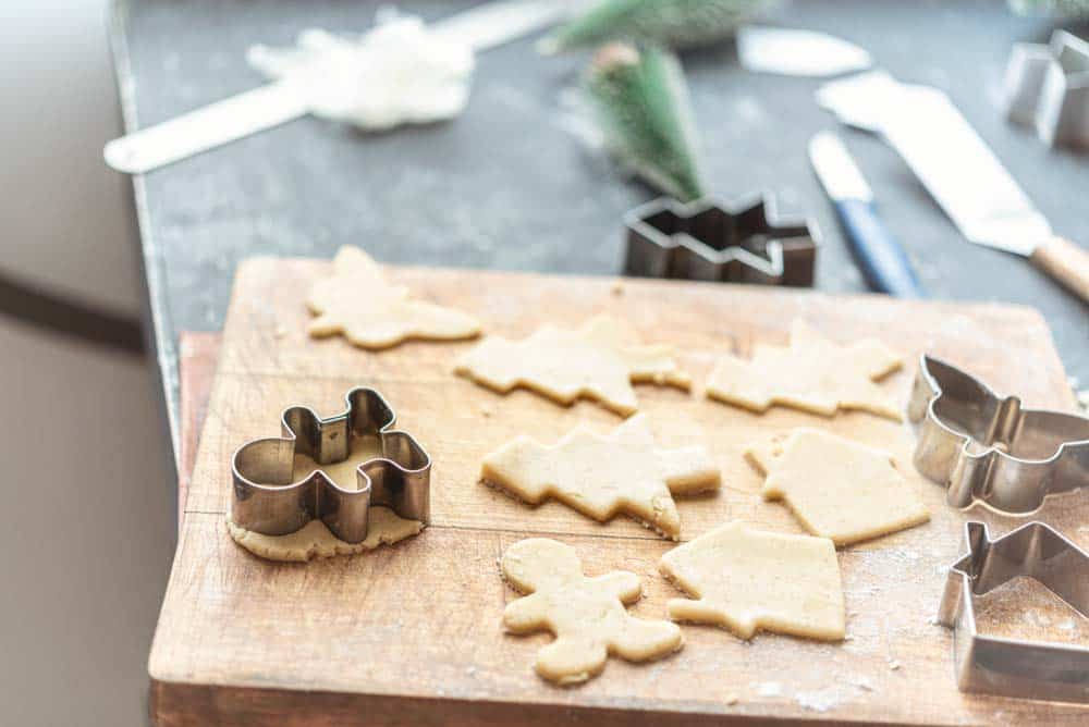 A wooden board with cut out Christmas cookie dough in tree and gingerbread person shapes