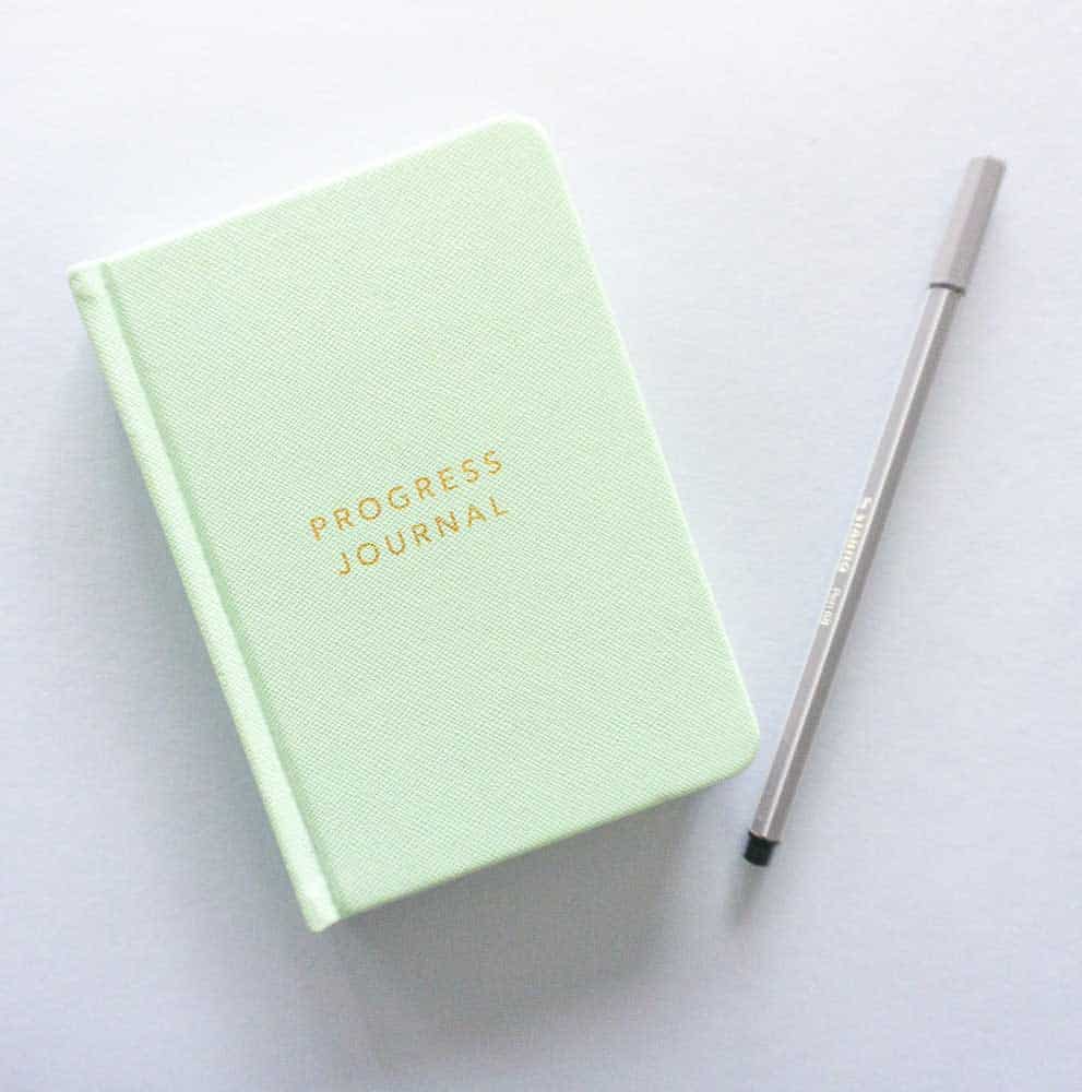 Green journal with gold embossed lettering that says Progress Journal